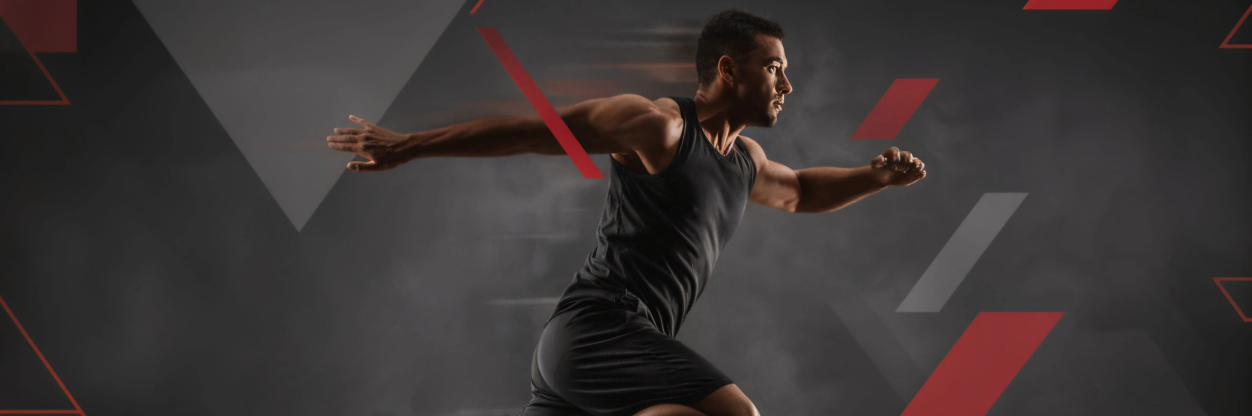 Un atleta masculino en plena carrera, con ropa deportiva negra, se mueve a alta velocidad contra un fondo abstracto de formas geométricas rojas y grises que sugiere movimiento y dinamismo.